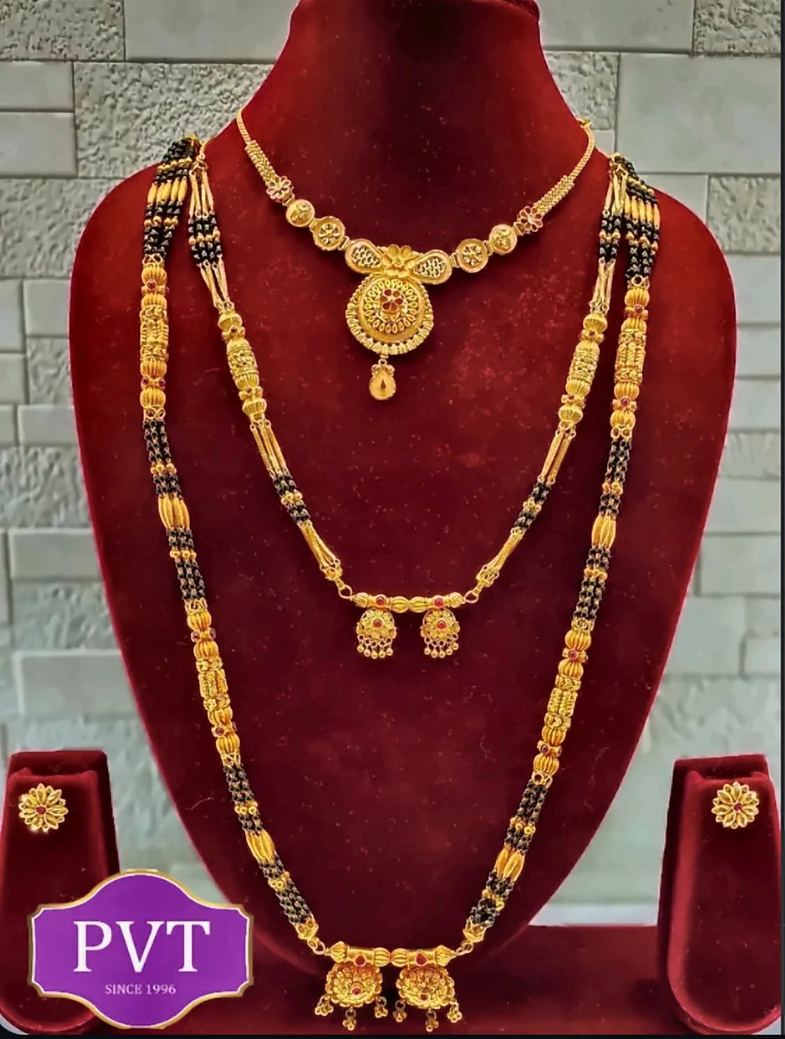 Gold mangalsutra and necklace set with black beads displayed on a red velvet bust, with matching earrings